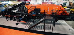 Eagle Crusher 8x20 Screening Plant at the Eagle Crusher booth at CONEXPO-CON/AGG. It is orange and black and features screen cloth, conveyor belt, platforms, and more.